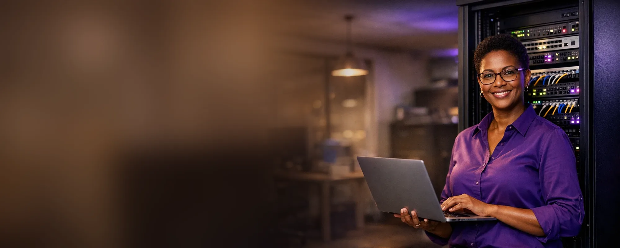 Gestora de TI sorrindo com o notebook ao lado do rack de rede da empresa